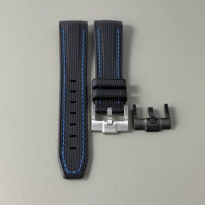 Puede incluir: Una correa de reloj negra con un patr&oacute;n de fibra de carbono texturizado y costuras azules. La correa incluye dos trabillas, una hebilla de metal plateado y un componente de hebilla de metal negro adicional para uso intercambiable.