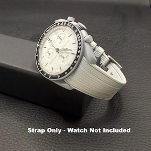 May include: A grey watch with a white face and a grey strap. The watch face has black and white details, including the word "Speedmaster". The strap has a textured pattern. The text "Strap Only - Watch Not Included" is at the bottom.