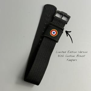Puede incluir: Una correa de reloj de nailon negro con una hebilla negra y una trabilla negra bordada con un emblema circular rojo, blanco y azul. El texto en la imagen dice: Limited Edition Version With Custom Black Keepers, con una flecha se&ntilde;alando.