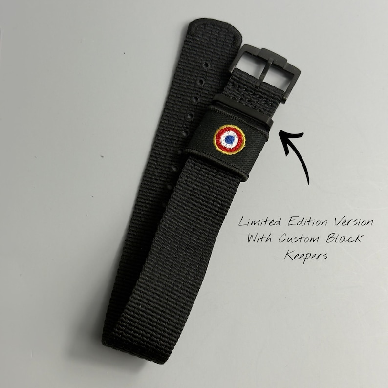 Puede incluir: Una correa de reloj de nailon negro con una hebilla negra y una trabilla negra bordada con un emblema circular rojo, blanco y azul. El texto en la imagen dice: Limited Edition Version With Custom Black Keepers, con una flecha se&ntilde;alando.