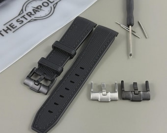 May include: A black watch strap with a textured surface, a black buckle, and a silver buckle. The strap is accompanied by a small screwdriver and a pouch with the text "THE STRAPOLOGIST".
