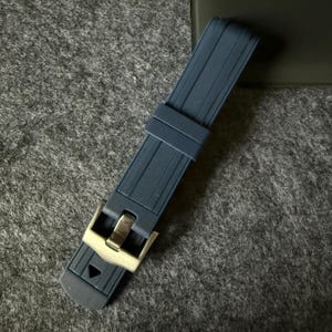 Puede incluir: Una correa de reloj azul marino con una hebilla de color plateado. La correa est&aacute; hecha de un material flexible y acanalado. La hebilla es rectangular con un acabado pulido.