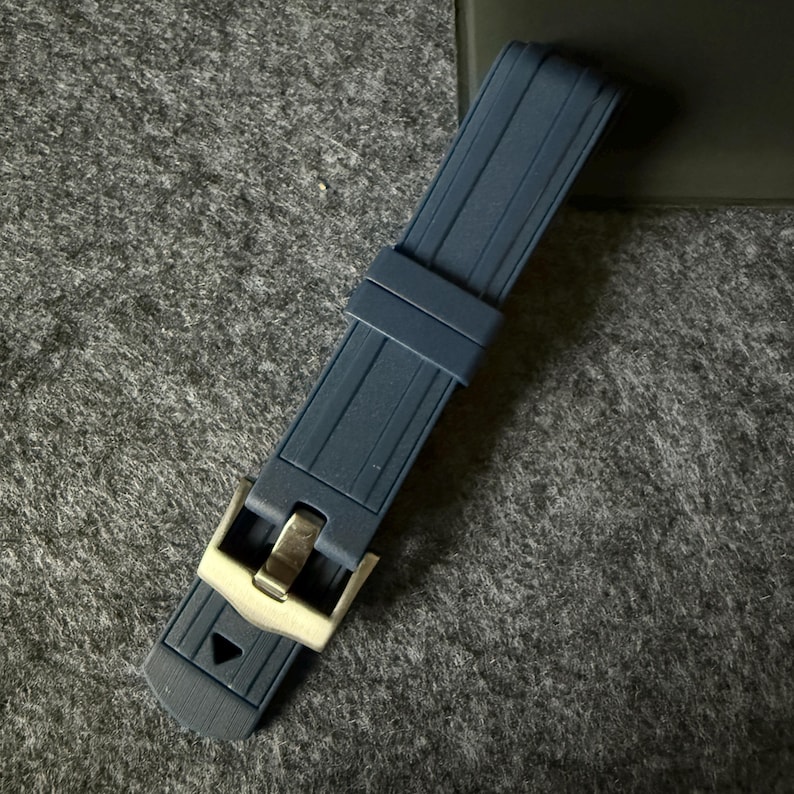 Puede incluir: Una correa de reloj azul marino con una hebilla de color plateado. La correa est&aacute; hecha de un material flexible y acanalado. La hebilla es rectangular con un acabado pulido.