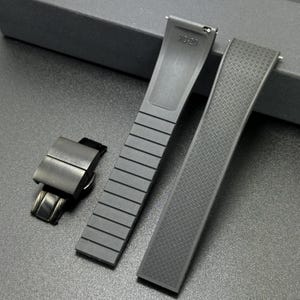 May include: A set of black watch straps and a clasp. One strap has a ribbed design, the other has a diamond pattern. The clasp is a folding type. The straps are marked "X0-20".