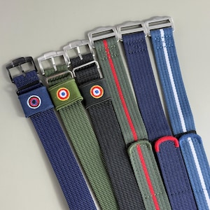 Puede incluir: Una colección de seis correas de reloj de nailon con diversos diseños. Dos correas incluyen parches circulares bordados, mientras que otras muestran rayas verticales en rojo, blanco o azul. Cada correa está equipada con una hebilla y herrajes de metal.
