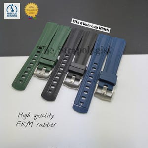 Op de afbeelding: Vier horlogebandjes in groen, zwart en blauw, gemaakt van hoogwaardig FKM-rubber. Elke band heeft een zilveren gesp en past op een bandaanzet van 21 mm. De tekst "The Strapologist" is zichtbaar.