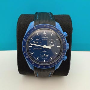May include: A blue and black Omega Speedmaster MoonSwatch watch with a black strap and a tachymeter scale around the bezel.