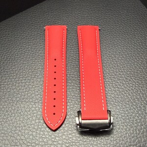 Puede incluir: Correa de reloj roja brillante con costuras blancas. La correa est&aacute; hecha de un material texturizado y presenta un cierre plateado. La correa est&aacute; dise&ntilde;ada para sujetarse a la esfera del reloj.