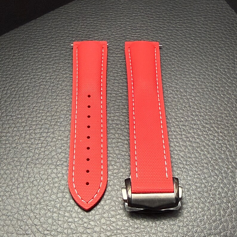 Puede incluir: Correa de reloj roja brillante con costuras blancas. La correa est&aacute; hecha de un material texturizado y presenta un cierre plateado. La correa est&aacute; dise&ntilde;ada para sujetarse a la esfera del reloj.