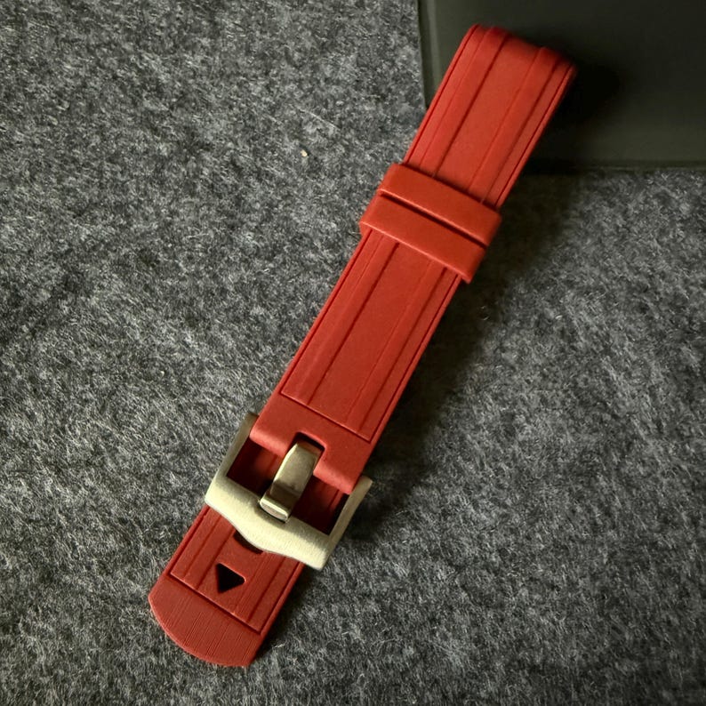 Puede incluir: Una correa de reloj roja con una hebilla plateada. La correa est&aacute; hecha de un material flexible y tiene una superficie texturizada. La hebilla es rectangular y tiene un dise&ntilde;o sencillo.