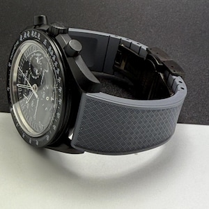 May include: A black wristwatch with a gray patterned band. The watch face is black with white and silver details, including multiple dials and hands. The watch has a sleek, modern design.