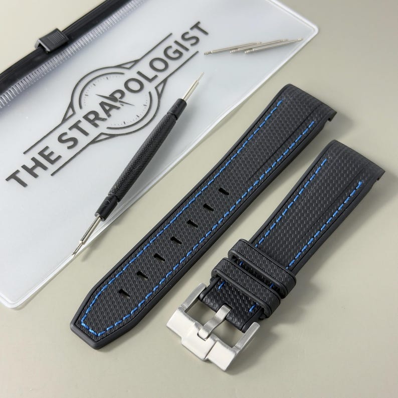 Puede incluir: Una correa de reloj negra con superficie texturizada y costuras azules, con una hebilla de metal plateado. Se incluyen una herramienta para pasadores negra y dos pasadores met&aacute;licos, junto a un estuche transparente con THE STRAPOLOGIST.