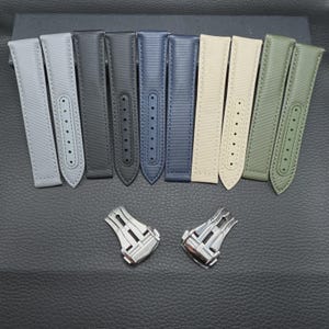 Könnte beinhalten: Eine Auswahl an Armbändern in verschiedenen Farben, darunter Grau, Schwarz, Marineblau, Beige und Olivgrün. Die Armbänder bestehen aus einem strukturierten Material und werden mit zwei silbernen Verschlüssen gezeigt.