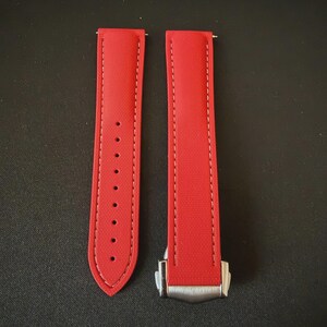 Puede incluir: Dos correas de reloj rojas brillantes con costuras blancas y un cierre plateado. Las correas est&aacute;n hechas de un material texturizado y tienen agujeros de ajuste. Las correas se muestran sobre un fondo oscuro.