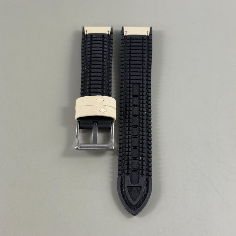May include: A black watch strap with a textured pattern. The strap has a cream-colored band and a silver buckle. The strap is designed to be durable and stylish.