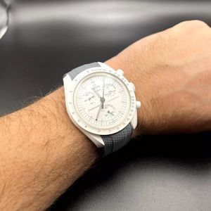 May include: A white and grey wristwatch with a chronograph function. The watch has a white face with black markings and a grey rubber strap.