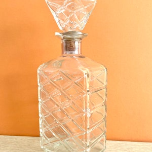May include: A clear glass decanter with a diamond-shaped stopper. The decanter has a square body with a textured, diamond-shaped pattern.