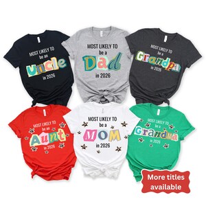 May include: A collection of six short-sleeved t-shirts in various colors, each featuring the phrase "MOST LIKELY TO be a" followed by a title like "Uncle" or "Mom" and the year "2026". The shirts are in black, gray, red, white, and green.