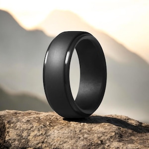 May include: A black silicone ring with a bevelled edge. The ring is sitting on a rock.