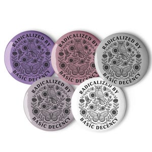 Peut inclure: Cinq badges ronds avec un motif floral et papillon, avec un hibou au centre. Les badges sont dans des tons de violet, rose, gris et blanc, avec le texte "RADICALIZED BY BASIC DECENCY" sur le bord.