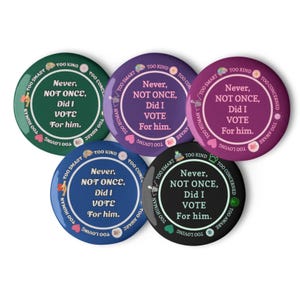 Puede incluir: Un conjunto de cinco botones redondos en varios colores: verde, morado, azul y negro. Cada botón presenta el texto "Never, NOT ONCE, Did I VOTE For him." y otras frases como "Too Smart" y "Too Human."