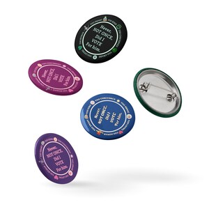 Op de afbeelding: Een verzameling politieke buttons in verschillende kleuren, waaronder zwart, paars en blauw. Elke button bevat de tekst "Never, NOT ONCE, Did I VOTE For him." en andere zinnen. De buttons hebben een speld.