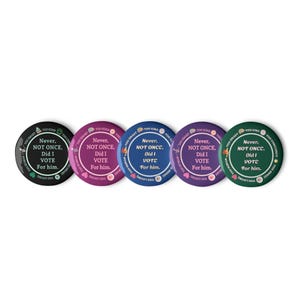 Op de afbeelding: Een verzameling van vijf ronde buttons in zwart, magenta, blauw, paars en groen. Elke button toont de witte tekst "Never, NOT ONCE, Did I VOTE For him." met extra tekst langs de rand. Een politieke boodschap.