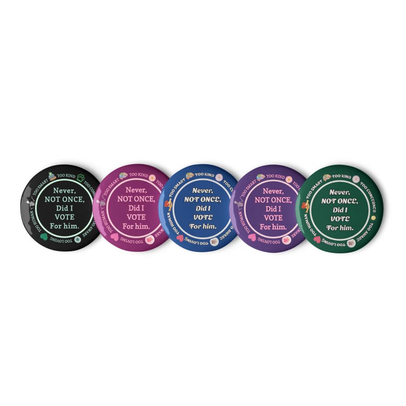 Op de afbeelding: Een verzameling van vijf ronde buttons in zwart, magenta, blauw, paars en groen. Elke button toont de witte tekst "Never, NOT ONCE, Did I VOTE For him." met extra tekst langs de rand. Een politieke boodschap.