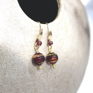 May include: A pair of gold dangle earrings with a burgundy glass bead and gold accents.