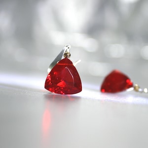Puede incluir: Un par de pendientes con piedras preciosas triangulares rojas y engastes plateados.