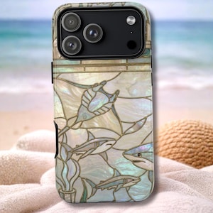 May include: An iPhone case with a pearlescent finish, showcasing a stained-glass design of sharks and seashells. The case has a black camera module and a protective bumper. The artwork includes white, blue, and gold hues.