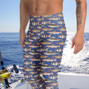 Könnte beinhalten: Blaue Leggings mit einem sich wiederholenden Muster aus Fischen in Braun-, Orange- und Weißtönen. Die Leggings werden von einer Person auf einem Boot getragen, mit einer Angelrute im Bild. Der Hintergrund zeigt das Meer und einen klaren blauen Himmel.