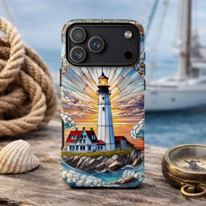 May include: A phone case featuring a lighthouse scene with a white tower, red roofed buildings, and a colorful sky. The case has a nautical theme, with a rope, seashell, and compass in the background.
