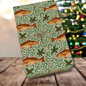 May include: A wrapped gift with a decorative paper featuring a repeating pattern of orange fish, green foliage, and red berries. The gift is tied with twine and set against a blurred Christmas tree background.