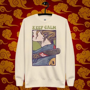 Könnte beinhalten: Ein cremefarbener Pullover mit langen Ärmeln und einem Rundhalsausschnitt. Die Vorderseite des Pullovers zeigt ein Grafikbild einer Frau mit einem Baseballschläger und dem Text "KEEP CALM" über dem Grafikbild. Das Grafikbild enthält auch den Text "F*CK OFF" und "SUP" auf dem Schläger.