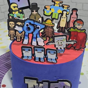 May include: A blue frosted cake with a red top, decorated with pixelated character cutouts. The cake has the name "TYLER" in silver letters. The cake is on a white plate with colorful polka dots.
