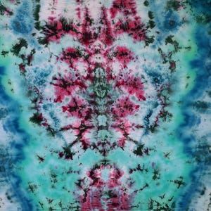 May include: A square, tie-dye textile with a symmetrical design. The pattern features a blend of colors, including shades of blue, teal, pink, and black. The design has a central floral-like motif, with radiating patterns.