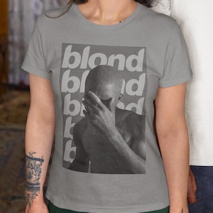 May include: Gray t-shirt with a black and white photo of a person with their face covered by their hand. The word "blond" is repeated in white text on the shirt.