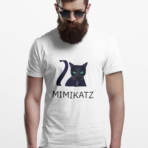May include: White t-shirt featuring a black cat graphic with green eyes and the text "MIMIKATZ" in a sans-serif font. The cat has a stylized design with a long tail. The shirt is worn by a person with a beard and sunglasses.