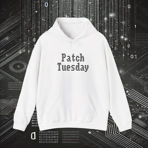 Puede incluir: Una sudadera con capucha blanca con un bolsillo delantero y un cordón. El texto "Patch Tuesday" está impreso en negro, con letras de bloque en la parte delantera. El fondo presenta un diseño de placa de circuito digital.