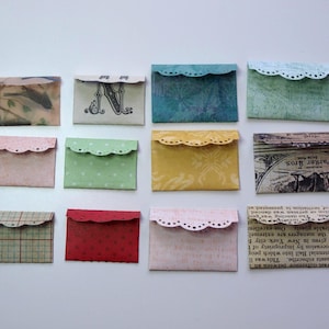 May include: A collection of twelve small, decorative paper envelopes with scalloped edges. The envelopes feature various patterns and colors, including floral, polka dots, and vintage text. Each envelope is approximately 3 inches wide.