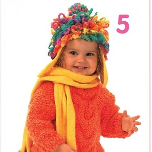 Può includere: Un bambino indossa un completo invernale fatto a mano. Include un maglione arancione brillante, una sciarpa gialla e un cappello colorato e strutturato. Il cappello e la sciarpa hanno dettagli in filato ad anello.
