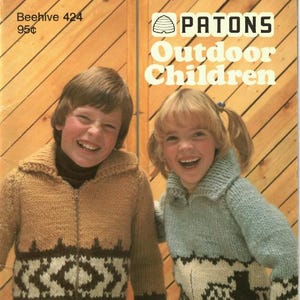 Puede incluir: Portada del libro de patrones de tejido Patons "Outdoor Children". Dos niños con jerséis de punto con cremallera y diseños geométricos. El jersey del niño es marrón y marrón, y el de la niña es azul y blanco. El texto "Plein air pour enfants" es visible.
