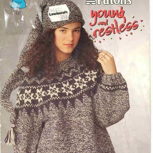 May include: A woman wearing a knitted sweater and hat. The sweater is a mix of gray and white with a geometric pattern across the chest. The hat has ear flaps and a tag that reads "46652 Lewiscraft 350". The words "Patons young and restless" are visible.
