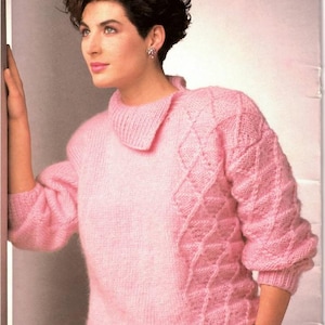 Puede incluir: Un suéter de punto rosa claro con un patrón de diamantes texturizado en el lado derecho y las mangas. El suéter tiene un cuello ancho y mangas largas. La modelo lleva pantalones grises oscuros. Es una fotografía de moda vintage.