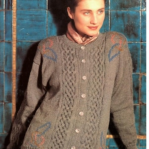 May include: A gray knitted cardigan with a cable knit design down the front and on the sleeves. The cardigan has a button-up closure and decorative patterns in blue, pink, and orange. The text "JAEGER" and "DOUBLE KNITTING" are visible.