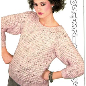 May include: A light pink knitted sweater with a round neckline and long sleeves. The sweater has a textured pattern and is paired with gray pants. The image is from a vintage fashion magazine.
