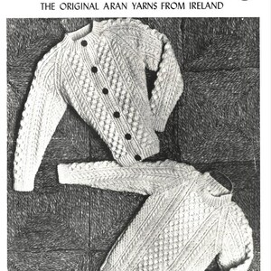 Può includere: Immagine in bianco e nero di due maglioni Aran. Il maglione superiore è un cardigan con bottoni neri. Il maglione inferiore è a girocollo. Il testo in alto recita "SPUN GOLD'S ARAN THE ORIGINAL ARAN YARNS FROM IRELAND".