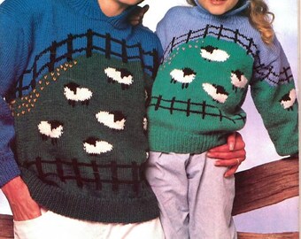 Op de afbeelding: Twee bijpassende blauwe en groene truien met schapenontwerpen. De truien hebben een coltrui en een landschapsscène met schapen en een hek. De truien worden gedragen door een vrouw en een kind, waarbij het kind een lichtblauwe broek draagt.