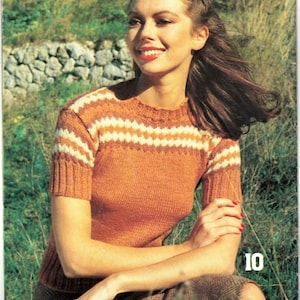 May include: An orange knit top with white and tan horizontal stripes on the sleeves and upper chest. The model is wearing a brown skirt and is sitting outside in a grassy area. The number 10 is visible on the right side of the image.